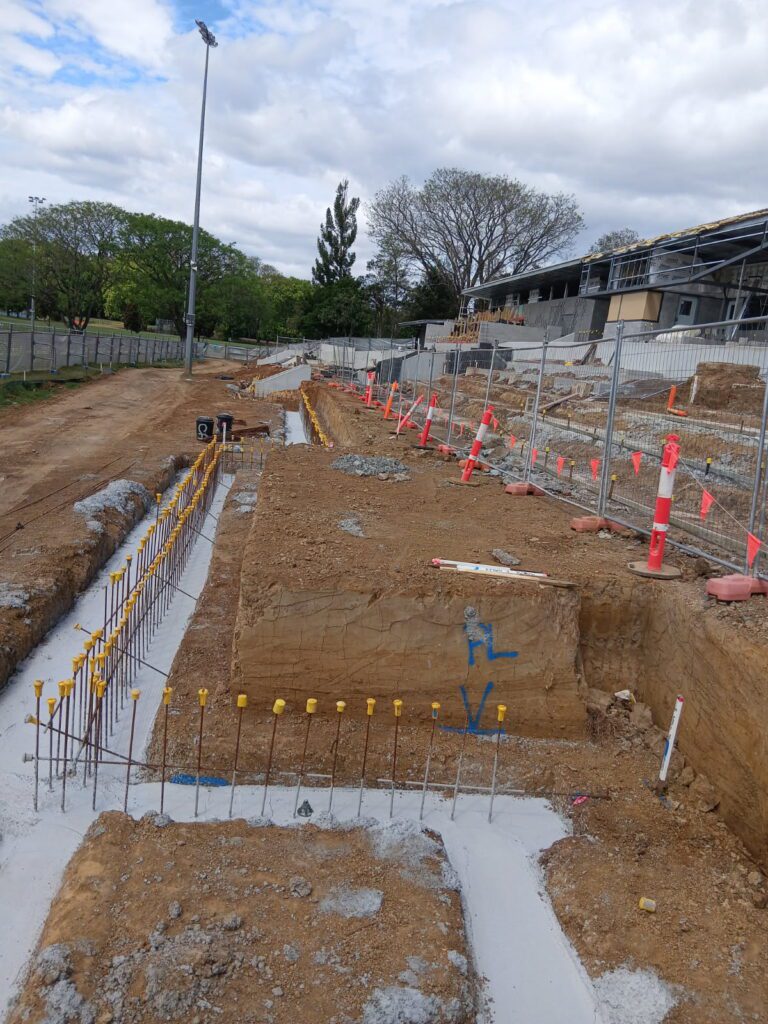 Reinforcing steel set out in excavated footings beside a sports grandstand